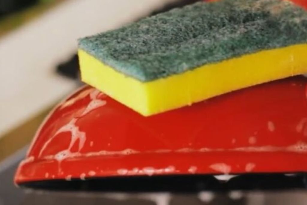 Mãos lavando uma panela Ceraflame com o lado macio de uma esponja amarela.